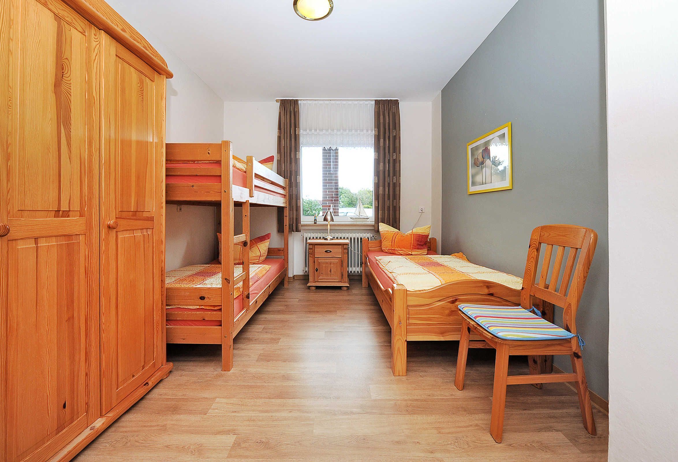 Une chambre avec des lits superposés, un bureau en bois, une chaise et un radiateur.