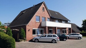 Une maison à deux étages, construite en briques, avec un toit en pente, un porche avant couvert et une allée où sont garées deux voitures.