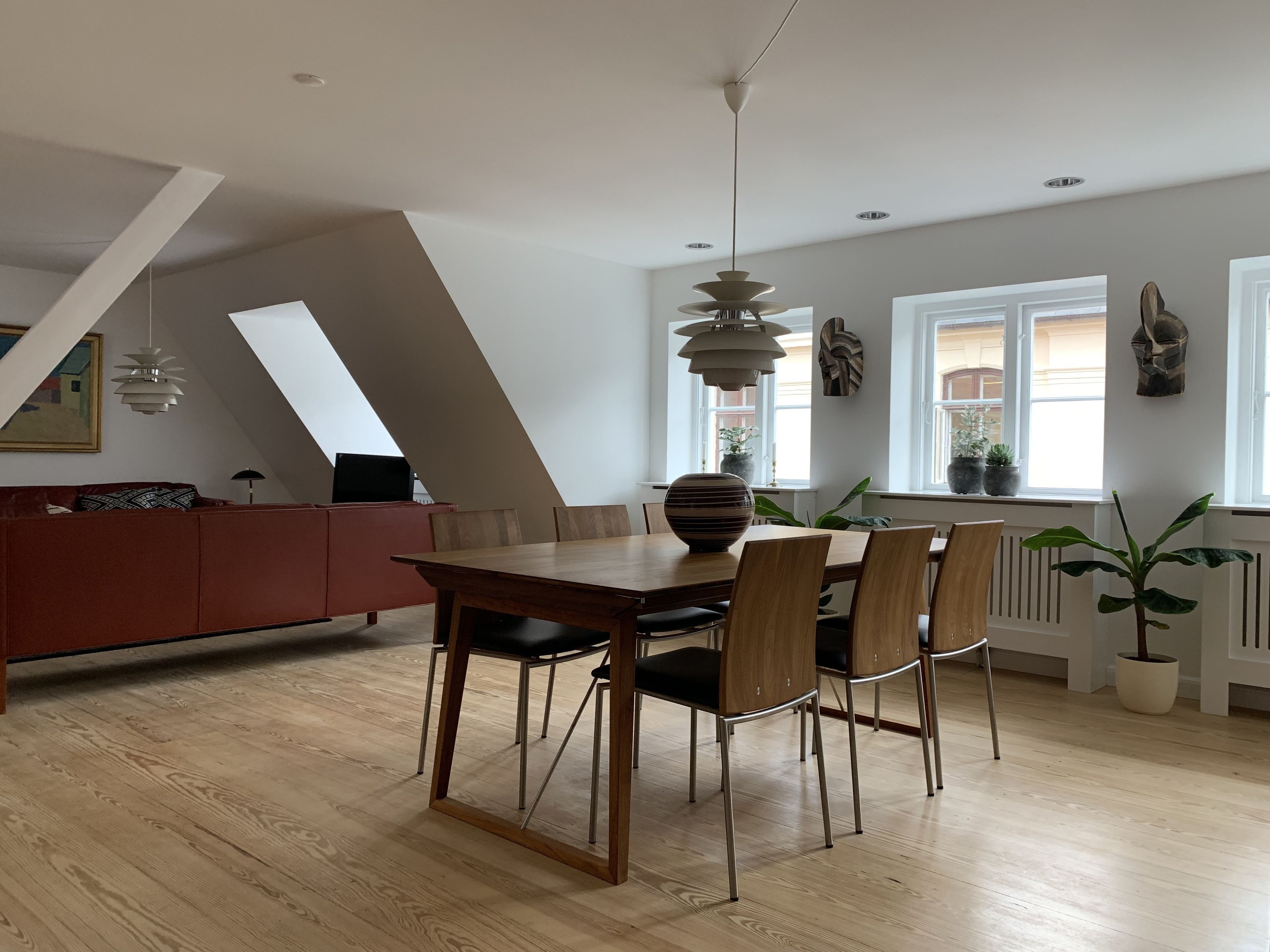 A modern dining area with a wooden table and chairs, a red sofa, and a pendant light.