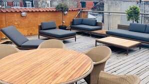 A rooftop terrace with wicker furniture, a round wooden table, and a view of the cityscape. - Best Stay Copenhagen Ny Adelgade 8-10 (Copenhagen)