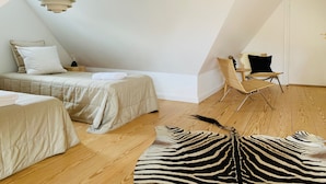A modern, minimalist bedroom with a sloped ceiling, a bed with a beige duvet, a chair, and a zebra-patterned rug. - Best Stay Copenhagen Ny Adelgade 8-10 (Copenhagen)