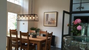 Un comedor con una mesa y sillas de madera, una lámpara colgante, un cuadro en la pared y un jarrón con flores.