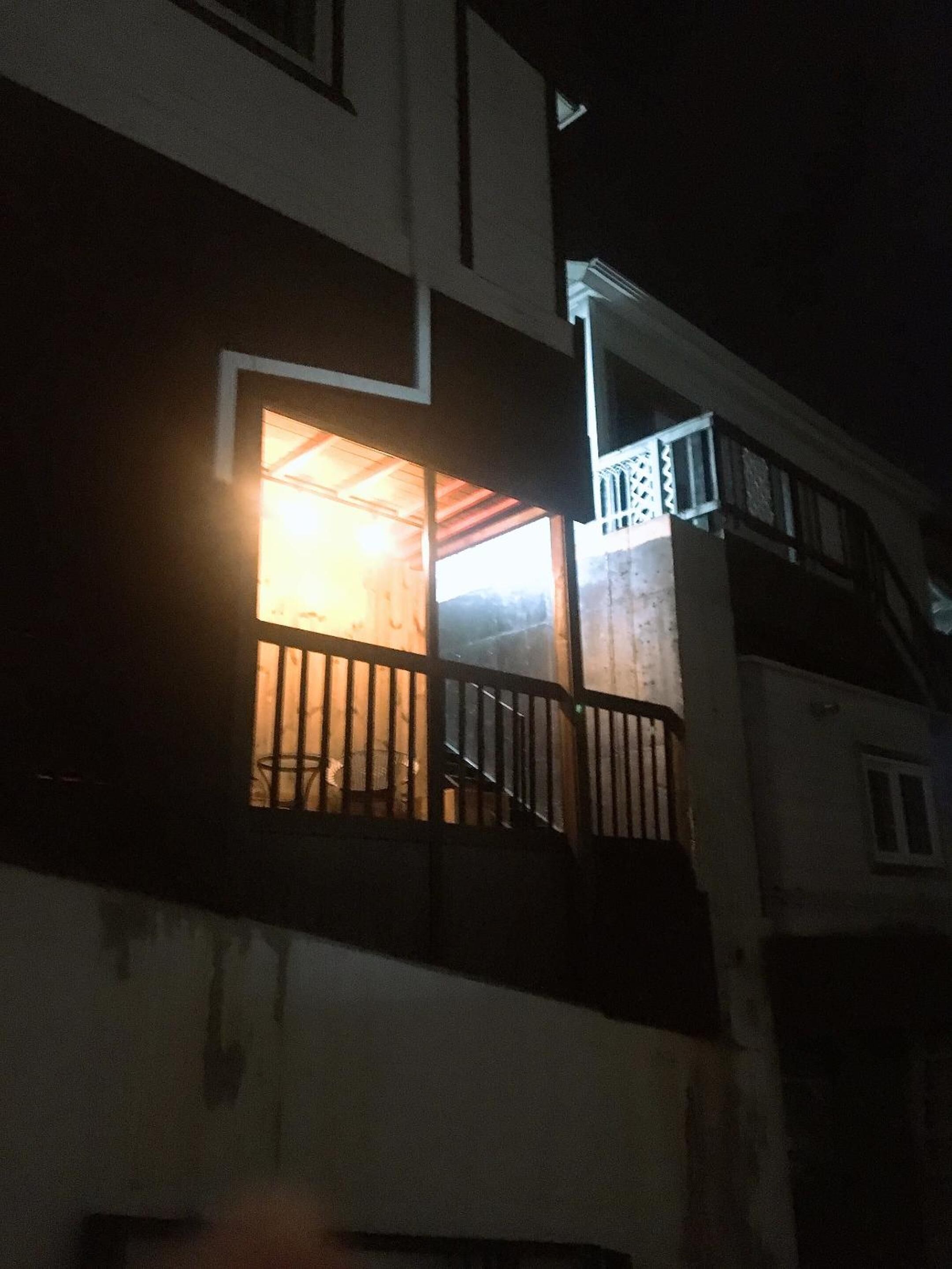 A building with a balcony and a lit window, suggesting an interior space.