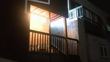 A building with a balcony and a lit window, suggesting an interior space.