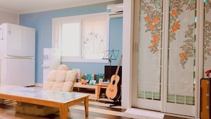 A living room with a sofa, a coffee table, a guitar, and a TV. - Hago Guest House (Tongyeong)
