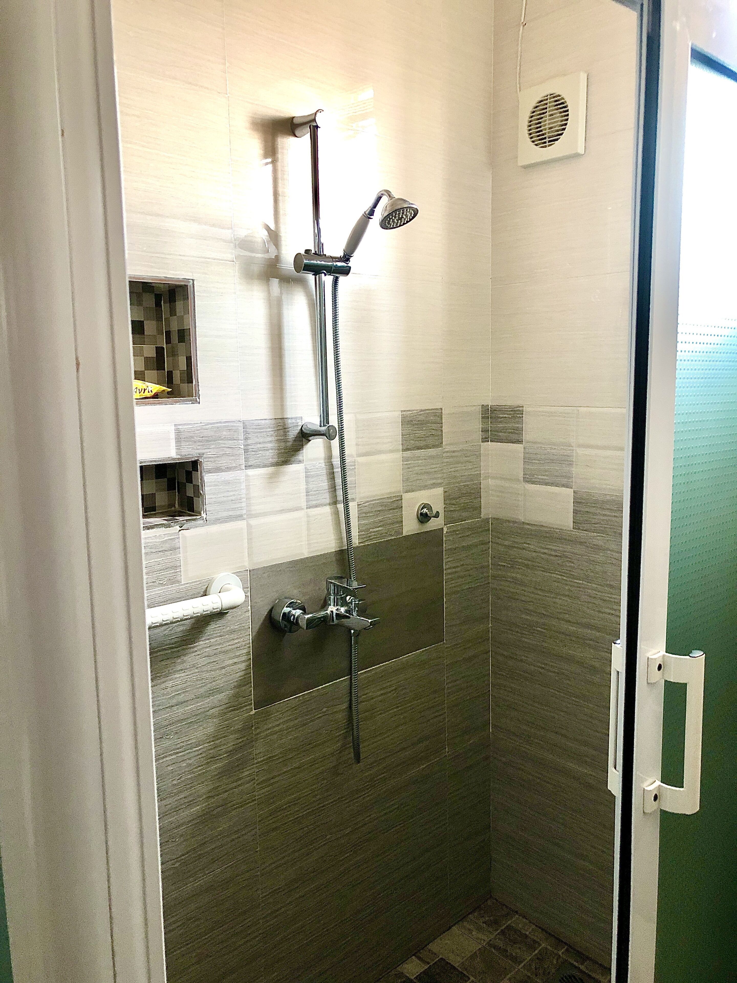 A small, enclosed shower area with a showerhead, handheld shower, and a control panel.