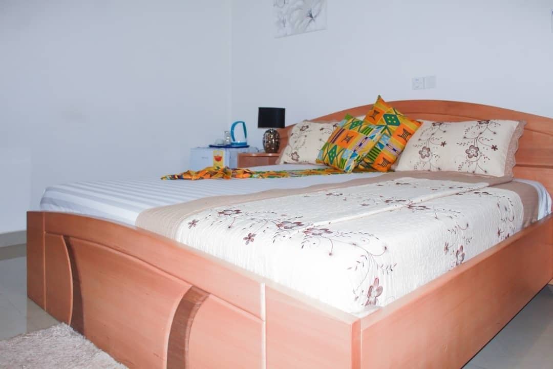 A neatly made bed with a floral bedspread, a wooden headboard, and colorful pillows.