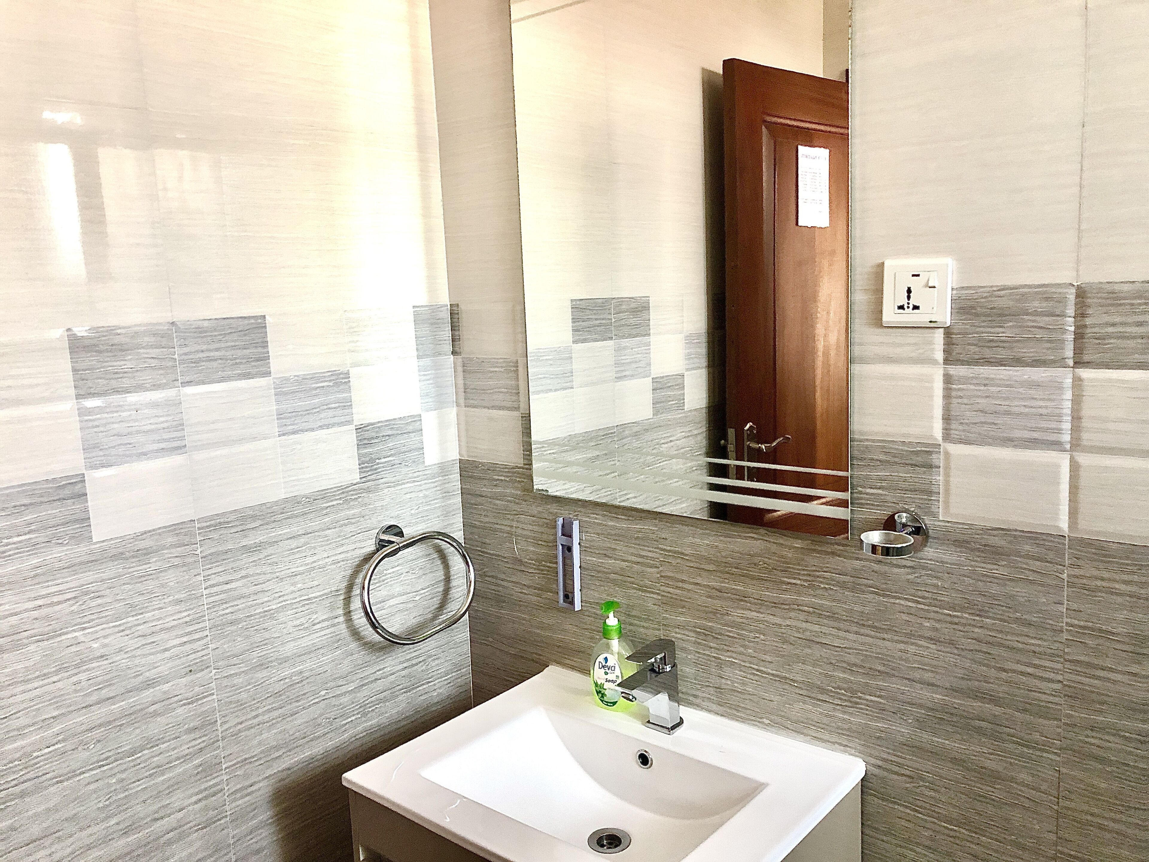 A bathroom with a sink, mirror, towel rack, and a bottle of Deva soap.