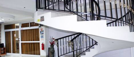 Un interior moderno con una escalera de caracol, una puerta de cristal y un florero con flores.