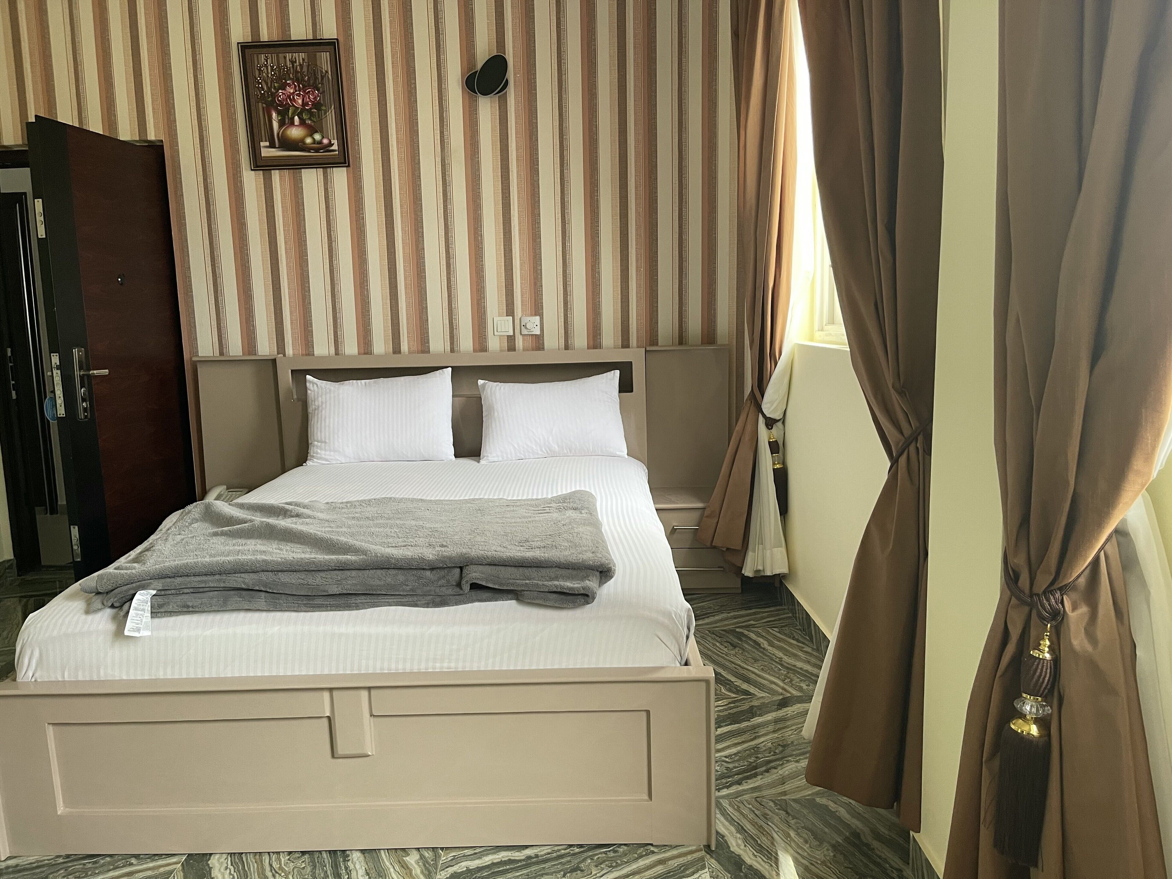 Habitación de hotel con cama, cortinas, un cuadro en la pared y una puerta.