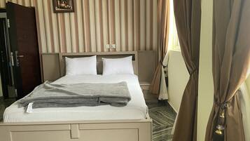 Habitación de hotel con cama, cortinas, un cuadro en la pared y una puerta.