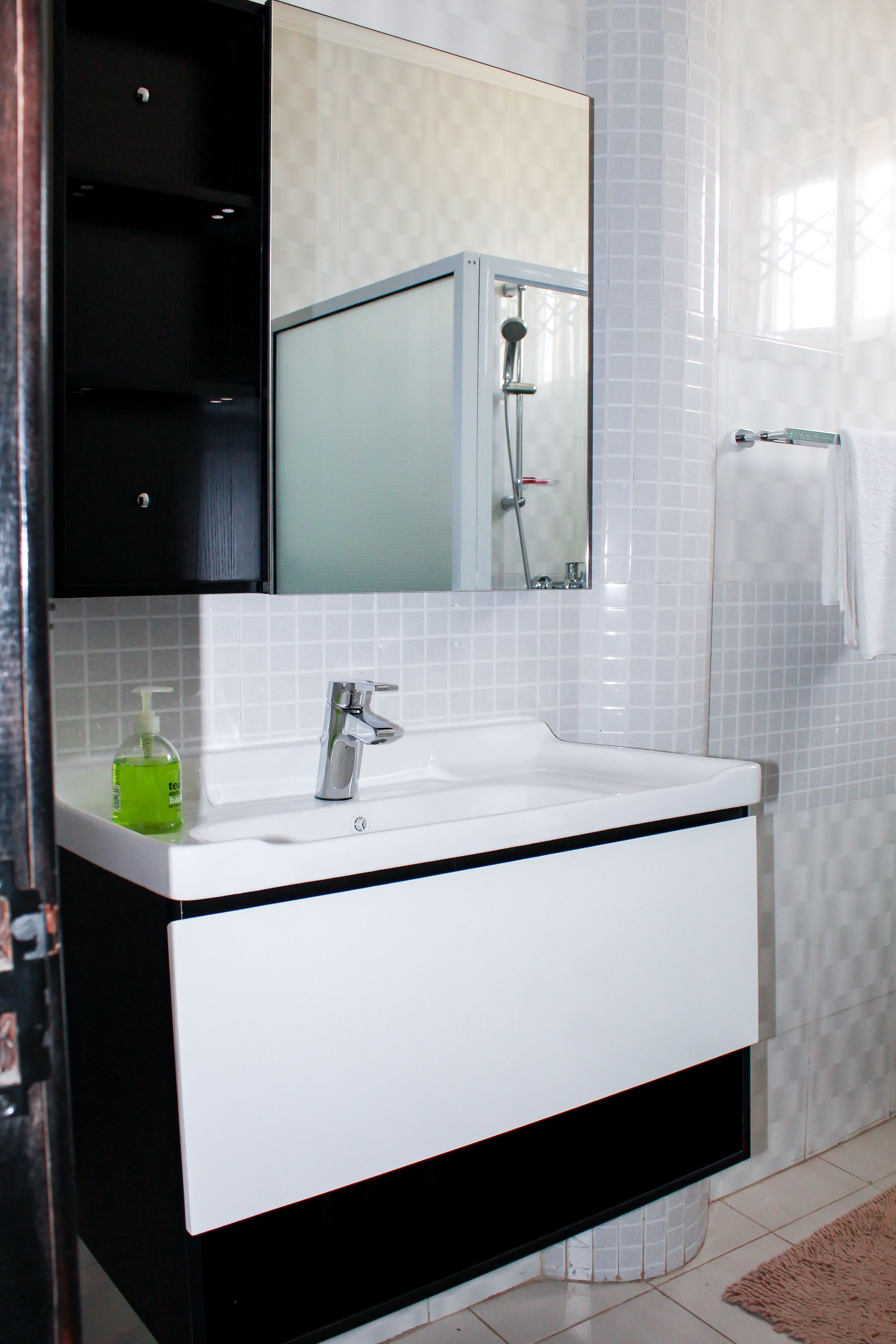 Een badkamer met een wit wastafelmeubel, een zwart kastje en een spiegel erboven.