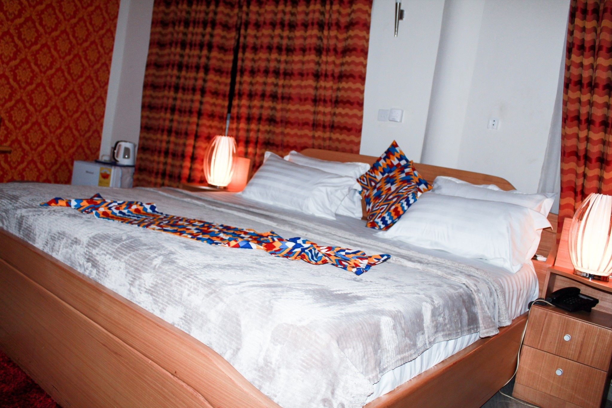 A hotel room with a large bed, a bedside table with a lamp, and a patterned curtain.