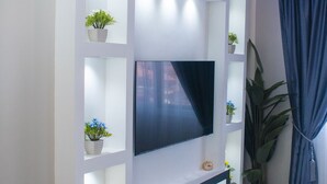 A modern living room with a flat-screen TV mounted on a white wall, surrounded by shelves with potted plants. - Exotic Palace Hotel (Accra)