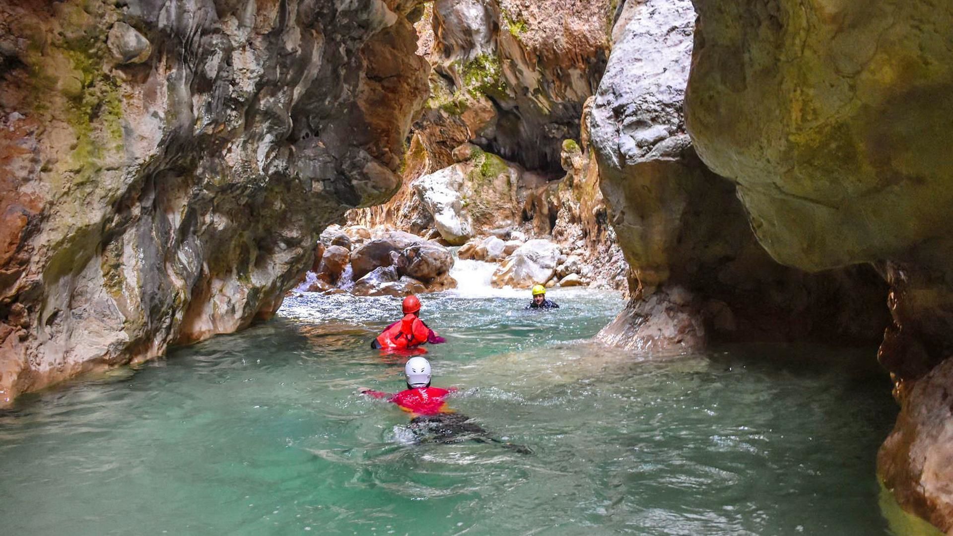 A narrow canyon with clear water, rocky walls, and kayakers.