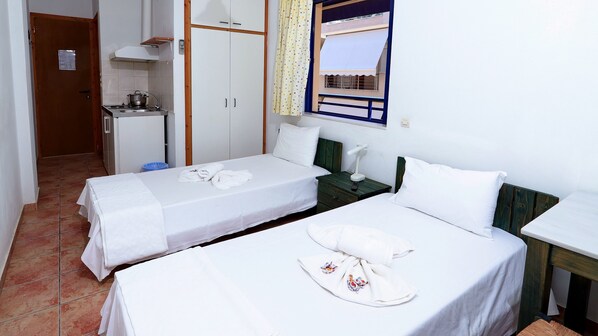 A room with two single beds, a small kitchenette, and a window with curtains.