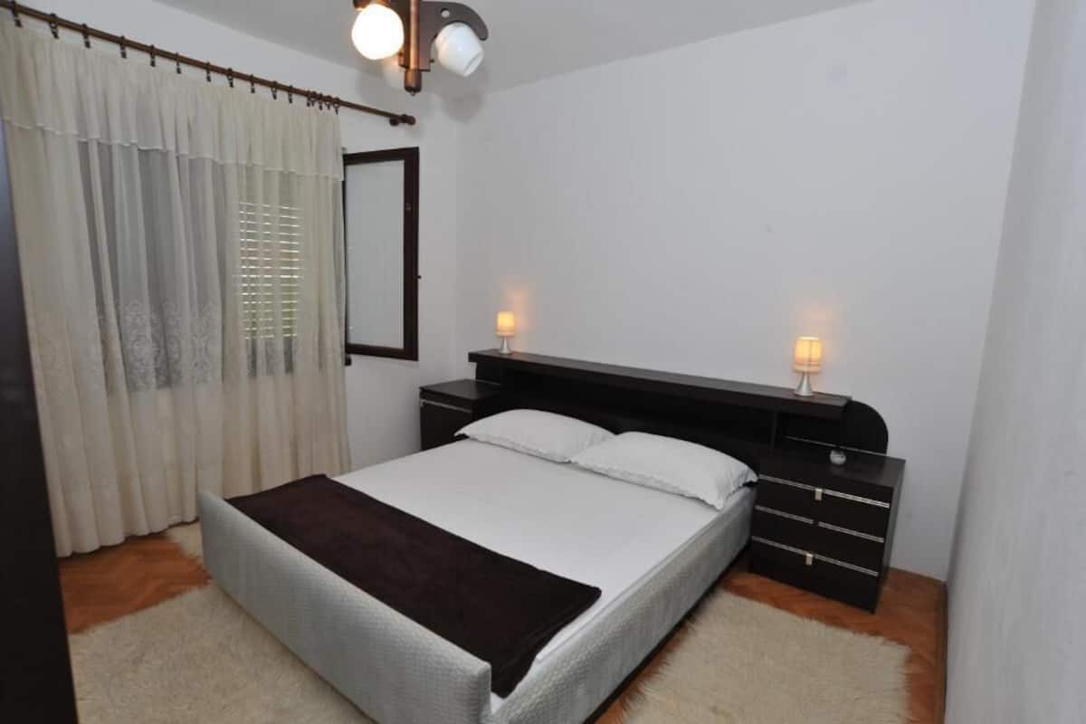 Une chambre à coucher comprenant un lit, une table de chevet, une commode, un miroir et une fenêtre avec des rideaux.