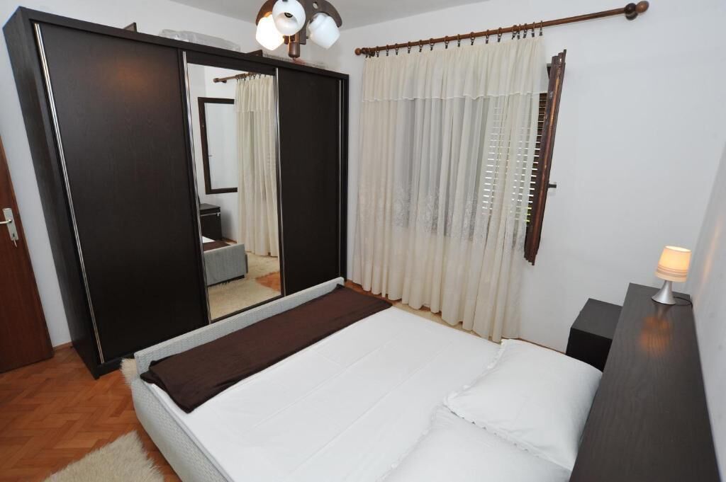 A bedroom with a bed, a wardrobe, a mirror, and a bedside table with a lamp.