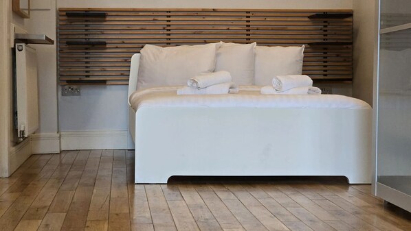 Un dormitorio moderno con cabecera de madera, cama blanca y suelo de madera.