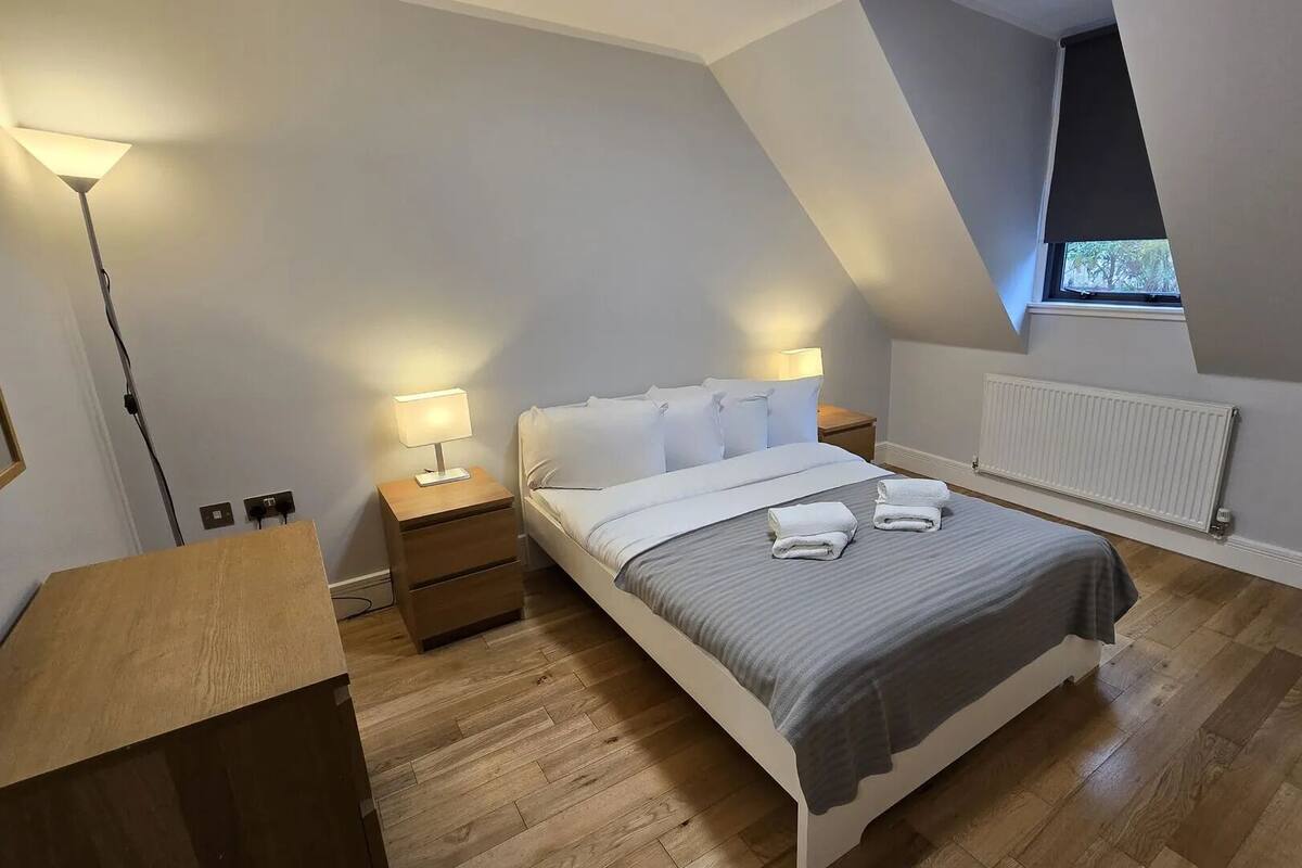 Un dormitorio moderno con cama, mesitas de noche, lámpara y ventana.