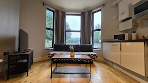Un espace de vie compact comprenant un canapé, une petite table avec une plante, un téléviseur et un coin cuisine.