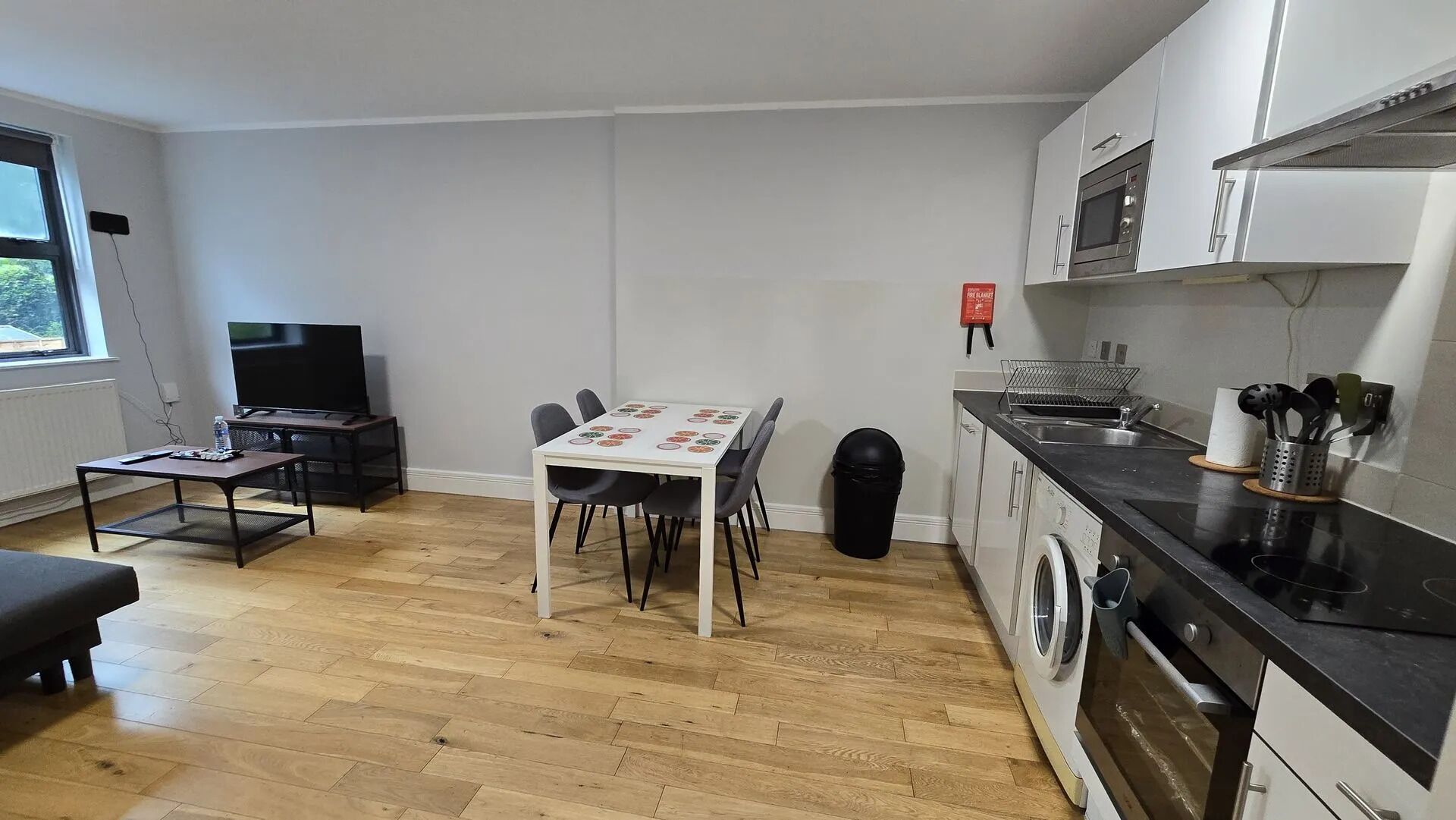 Una cocina funcional con lavadora, una mesa de comedor con sillas, un televisor y una ventana.