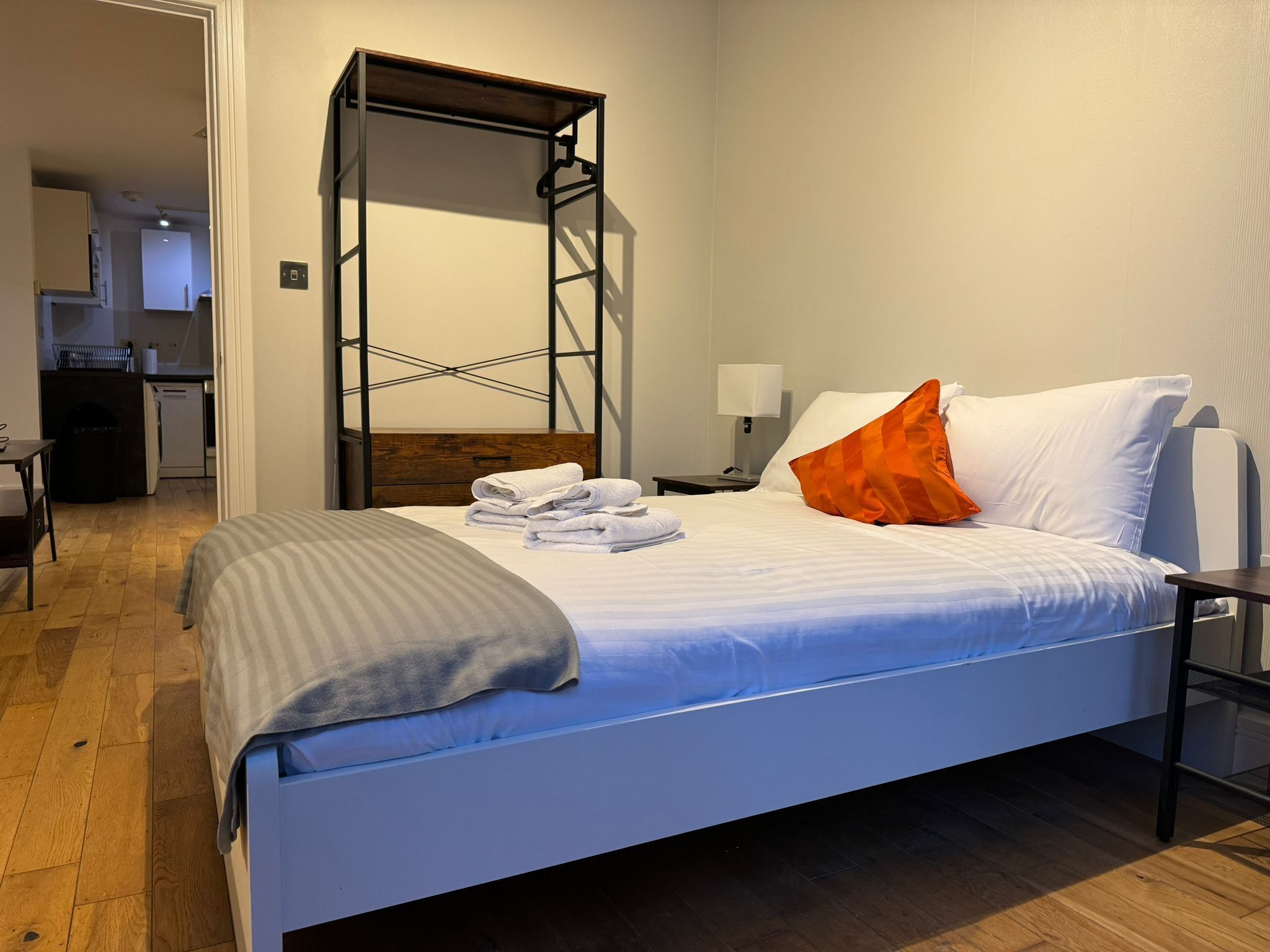 Et moderne hotelværelse med seng, træsengkag, et natbord, en lampe og udsigt til køkken og opholdsstue.