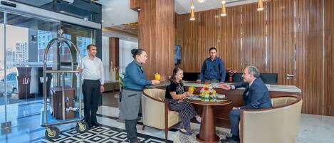Um hall de hotel moderno com uma grande mesa redonda, área de recepção e vista da cidade através de amplas janelas.