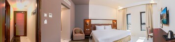 Una habitación de hotel con cama, una silla, un escritorio con cafetera y un televisor en la pared.