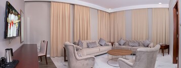 Egy modern nappali, melyben bézs színű kanapé található, egy fa kávézóasztallal és egy a falra szerelt televízióval.