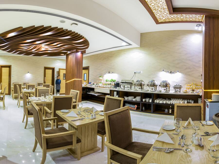 A modern dining area with multiple tables and chairs, a central buffet, and a decorative ceiling.