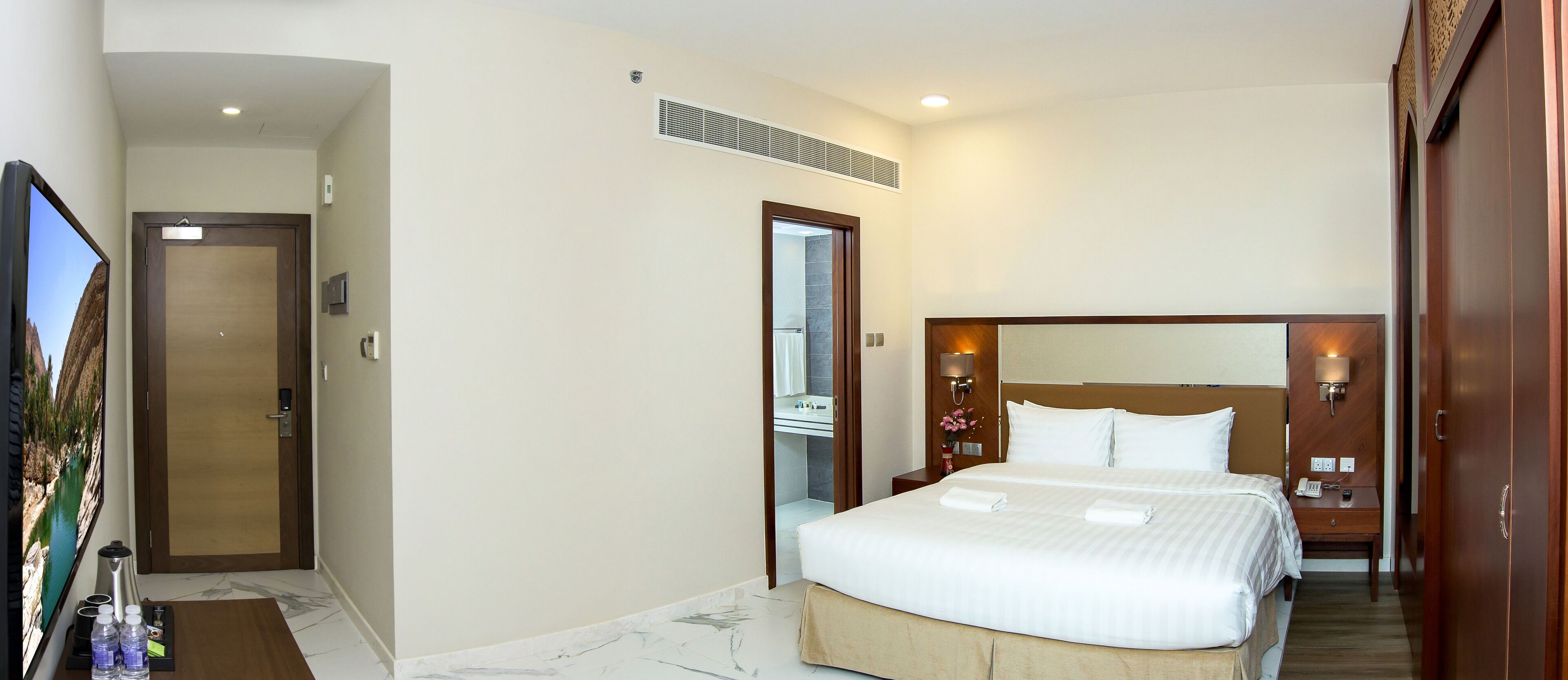 A hotel room with a large bed, a television, a bathroom, and a wooden wardrobe.
