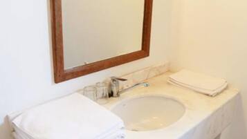 Un baño con un lavamanos de mármol blanco, un espejo con marco de madera y una pila de toallas blancas sobre el mostrador.