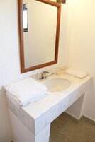 Un baño con un lavamanos de mármol blanco, un espejo con marco de madera y una pila de toallas blancas sobre el mostrador.
