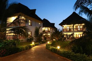 A pathway leading to a resort with multiple buildings, each featuring balconies and surrounded by lush greenery.