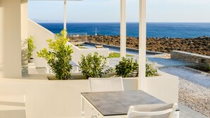 Eine Terrasse im Freien mit Tisch und Stühlen, mit Blick auf eine felsige Küstenlinie und das Meer.