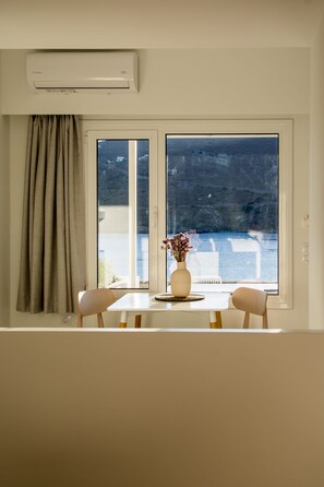 A room with a large window, a table with two chairs, a vase with flowers, and an air conditioning unit.