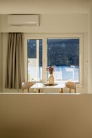 Una habitación con un ventanal grande, una mesa con dos sillas, un florero con flores y un equipo de aire acondicionado.