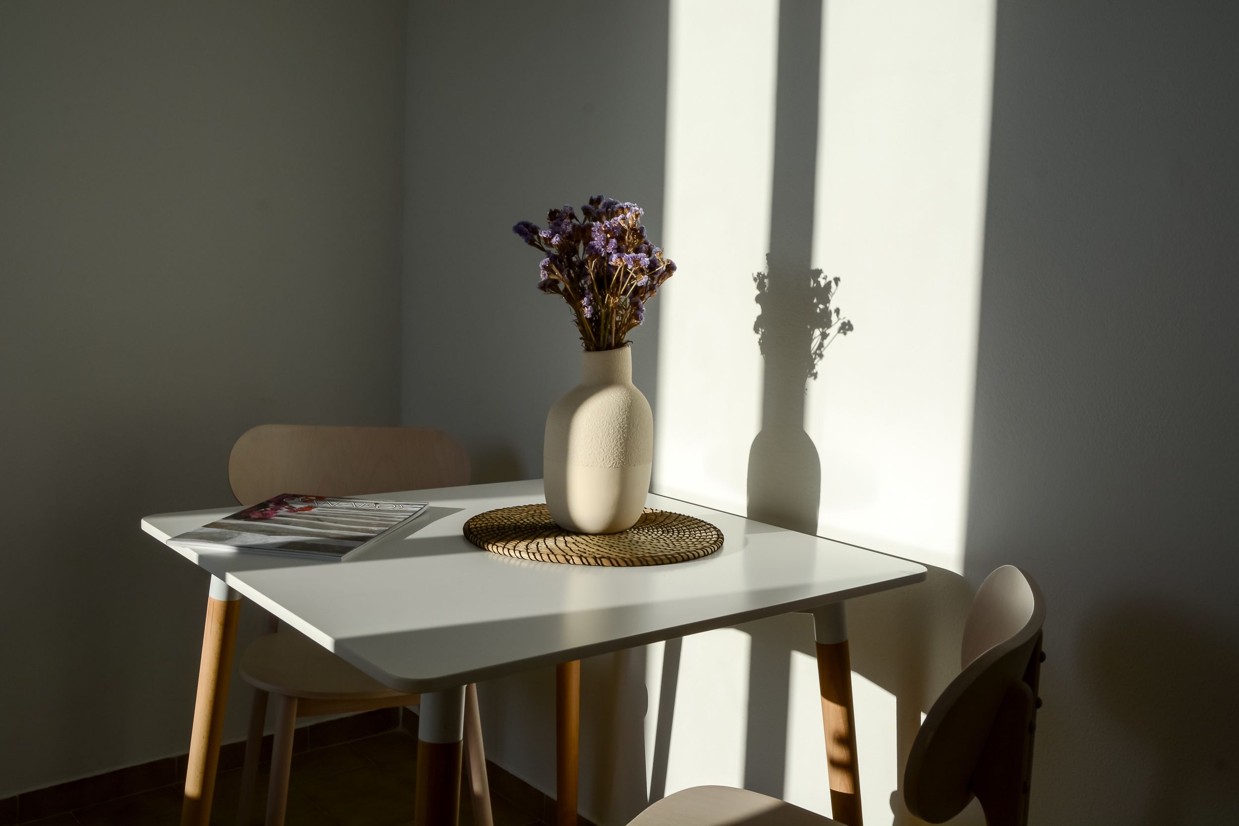 A dining table with a vase of flowers, a placemat, and a magazine.