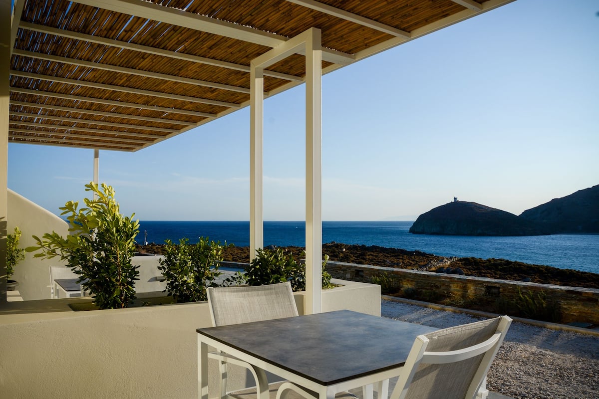 A covered outdoor seating area with a view of the sea and rocky coastline.