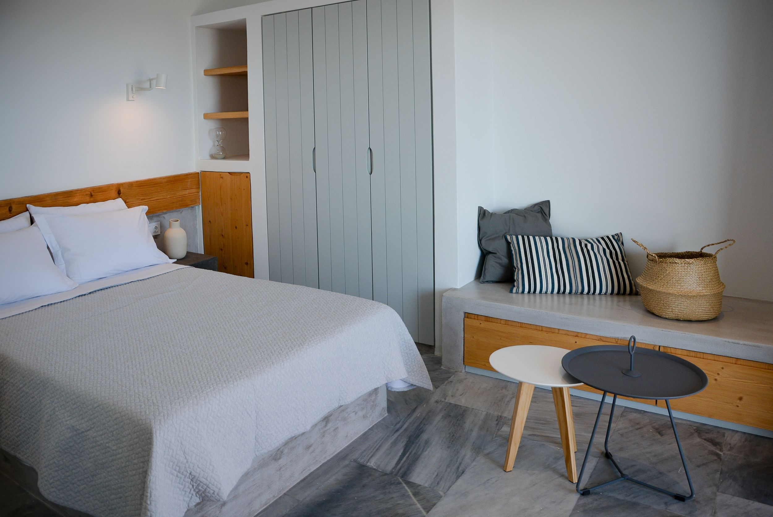 A bedroom with a bed, a bench with cushions, a small table, and a wardrobe.