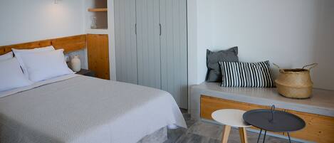 A bedroom with a bed, a bench with cushions, a small table, and a wardrobe.