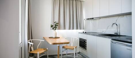 A compact kitchen with white cabinets, a built-in oven, a sink, and a dining area with two chairs and a table.