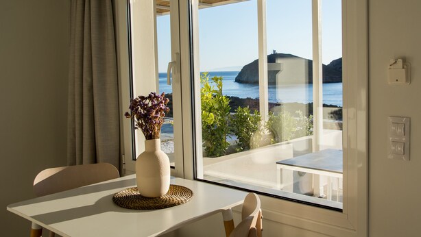 Ein Zimmer mit Meerblick, ein Tisch mit Blumen in einer Vase und ein Fenster mit Vorhängen.