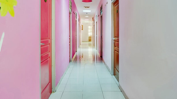 Um corredor bem iluminado, com paredes rosa e chão de azulejos brancos, que leva a uma porta no final.