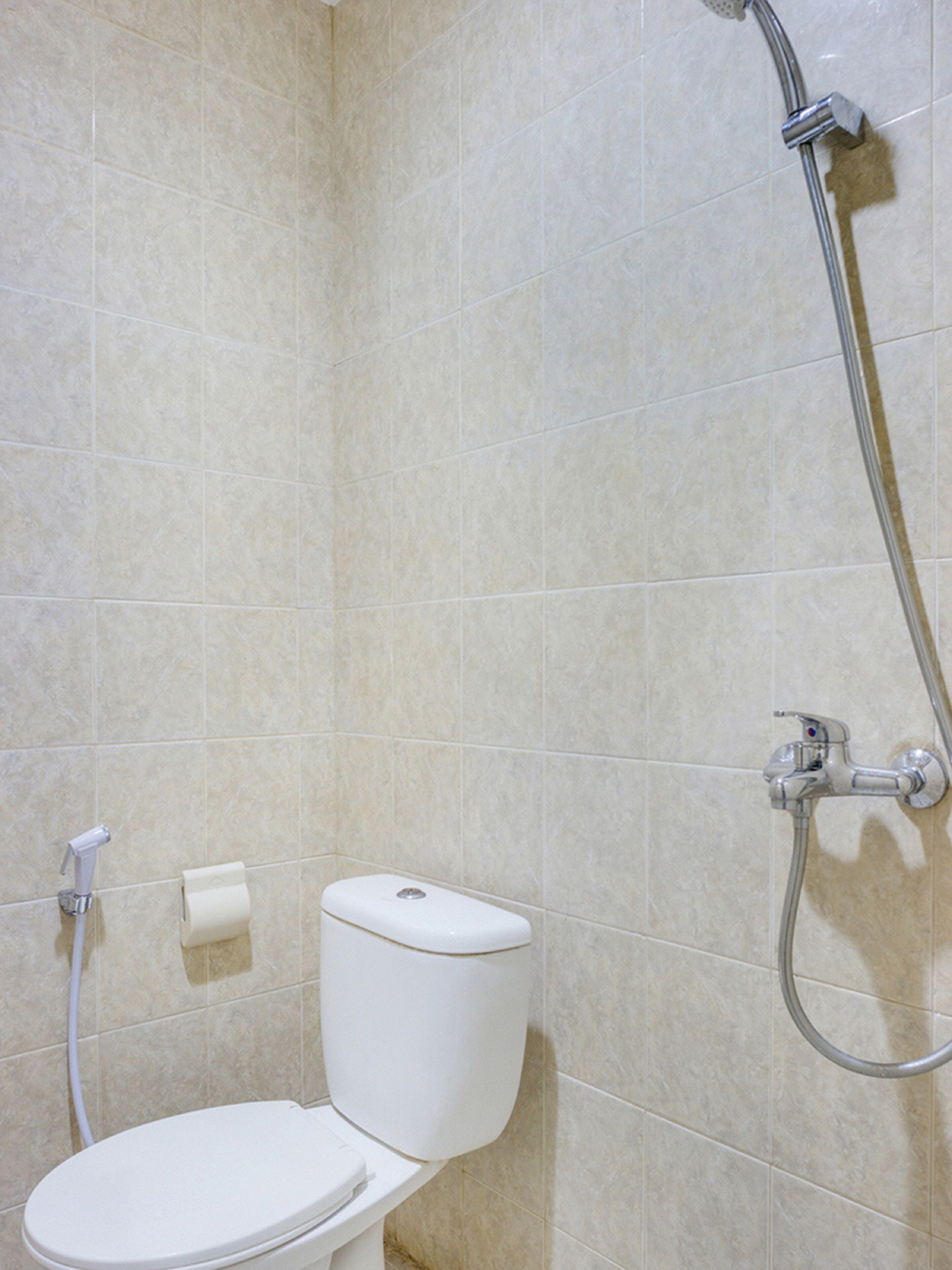 Un baño con inodoro, ducha y un rollo de papel higiénico en la pared.