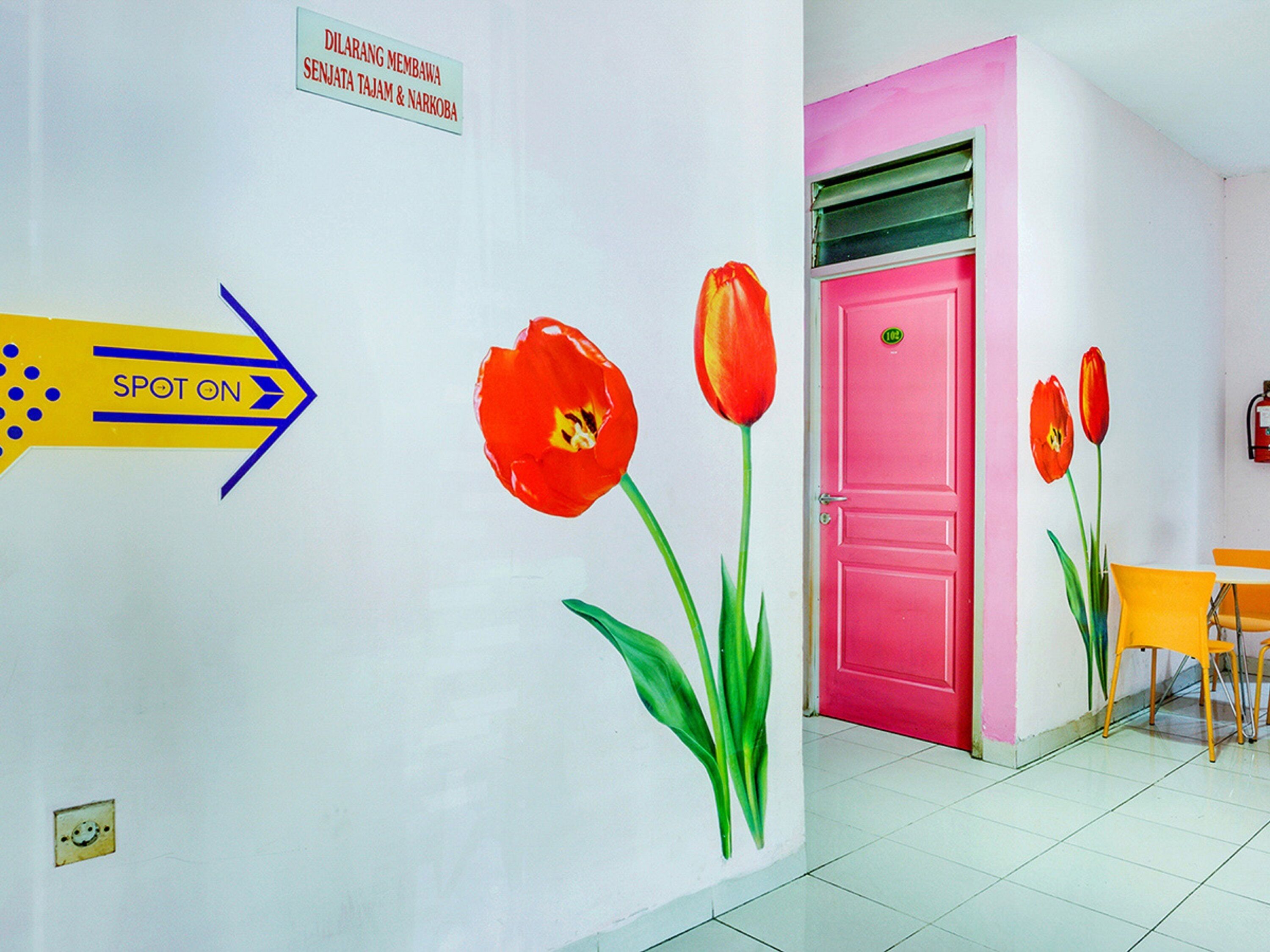A hallway with a sign indicating the location of the room, a pink door, and a yellow chair.