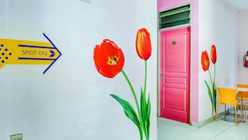 A hallway with a sign indicating the location of the room, a pink door, and a yellow chair.