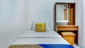 Um quarto pequeno e bem arrumado com uma cama de solteiro, mesa de cabeceira, espelho e guarda-roupa.