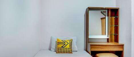 Un dormitorio pequeño y ordenado con una cama individual, una mesita de noche, un espejo y un armario.